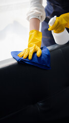 Person cleaning the room, cleaning staff is using cloth and spraying disinfectant to wipe the sofas...