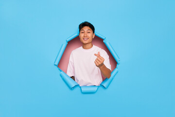 Cheerful positive asian young man keeps palm raised near the mouth and scream loudly poses through...