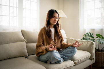 Young asian woman hand meditating and sitting on couch in living room at house
