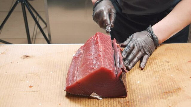 Close-up of the process of cutting tuna fish at the market. Male hands in gloves cutting a large fish with a knife.