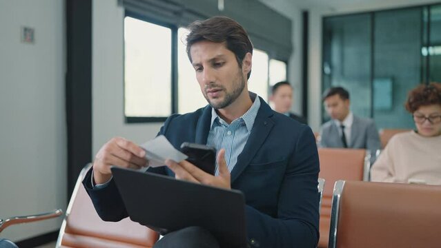 Indian businessman using smartphone sitting recheck boarding pass waiting for flight and working on laptop at airport terminal