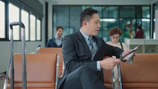 Asian businessman sitting and recheck boarding pass waiting for flight using lablet typing and working at airport terminal