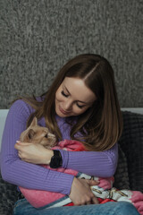 A young woman in her bedroom holds her pet cat wrapped in a baby blanket in her arms. Love and care for animals, childless woman. Treating animals like your children