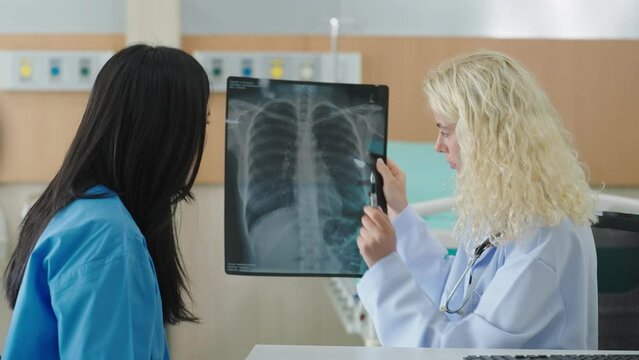 Professional caucasian woman doctor talking with woman patient about x-ray film with lung pneumonia caused by infection at clinic. Covid-19 xray test, covid worldwide virus epidemic