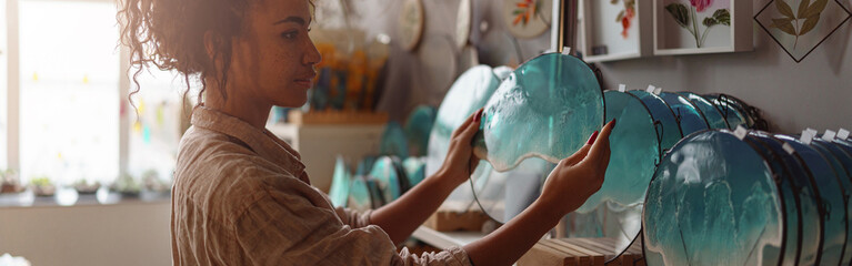 Woman decorator puts handmade epoxy resin glass tray with sea waves on stand in art studio - obrazy, fototapety, plakaty