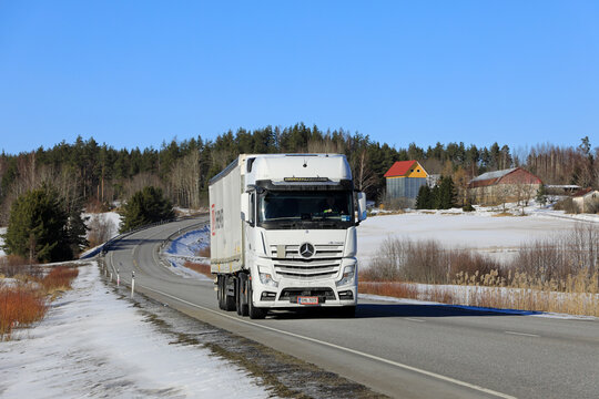 Road landscape with White Mercedes-Benz Actros 2653 truck in front of DB Schenker semi trailer on a sunny day of early spring. 