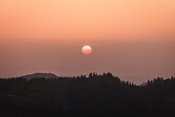 Sonnenglanz im Abendrot: Silhouettenhügel und die strahlende Sonne im Sonnenuntergang