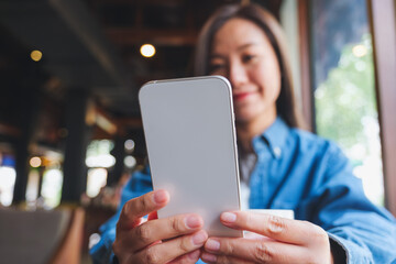 Blurred image of a young woman holding and using mobile phone in cafe