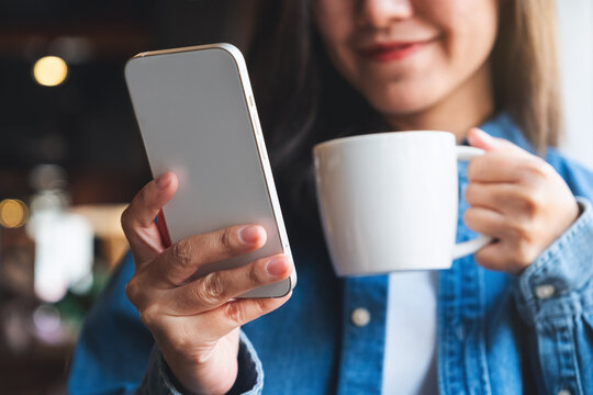 Closeup image of a young woman holding and using mobile phone while drinking coffee in cafe