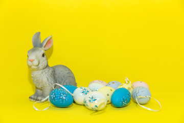 Easter bunny sitting among multicolored eggs isolated on yellow background. Easter bunny rabbit with colorful eggs, holiday concept