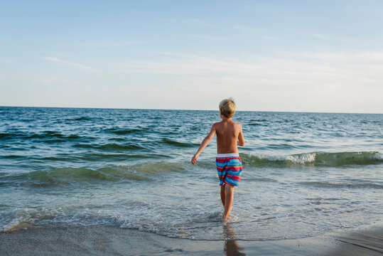 Rear view of shirtless boy walking at Tobay Beach towards sea against sky