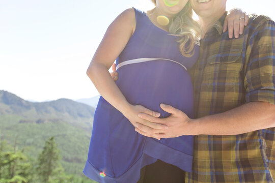 Man touching pregnant woman's stomach while standing against mountains during sunny day