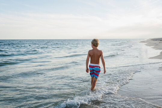 Rear view of shirtless boy walking at Tobay Beach in waves against sky