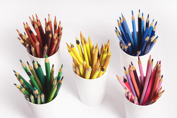 colored pencils in white glasses on a white background. Top view photo of stacks of pencils by...
