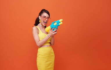 cheerful tourist woman traveling with water gun during Songkran festival studio on copy space orange background.