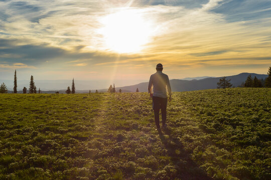 Rear view of hiker walking on field against cloudy sky during sunny day