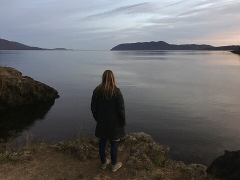 Woman wearing jacket while looking at view by river against sky