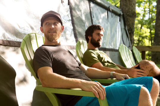 Friends sitting on chairs while relaxing by tent at campsite in forest
