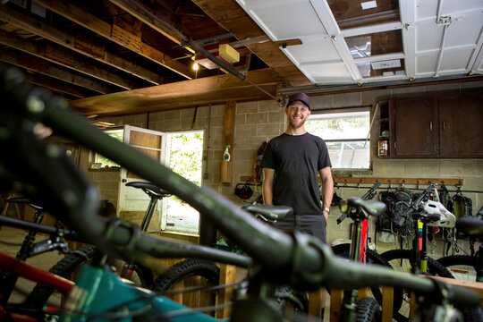 Low angle portrait of confident mechanic with hands in pockets standing in bicycle shop