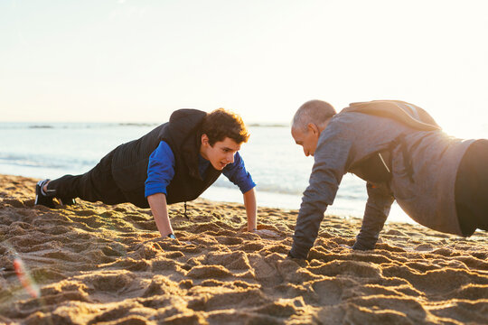 Determined father and son doing push-ups together against clear sky at beach during sunset