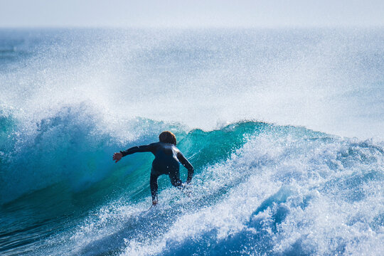 Rear View Of Teenage Boy Surfing In Sea