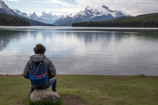 Hiker with backpack looking at view while sitting on rock by Maligne Lake