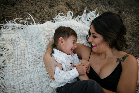 High angle view of playful mother tickling son while lying on picnic blanket