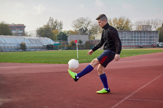 Full length of teenage boy playing with ball at running track against sky