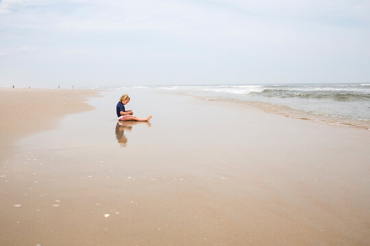 Side view of girl playing while sitting on shore at beach against sky