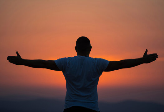 Rear view of carefree man with arms outstretched standing against sky during sunset