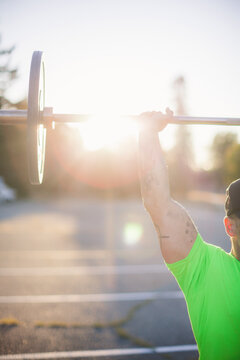 Cropped image of man lifting barbell during sunny day at park