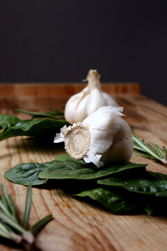 Garlic bulbs with spinach on wooden table against black background