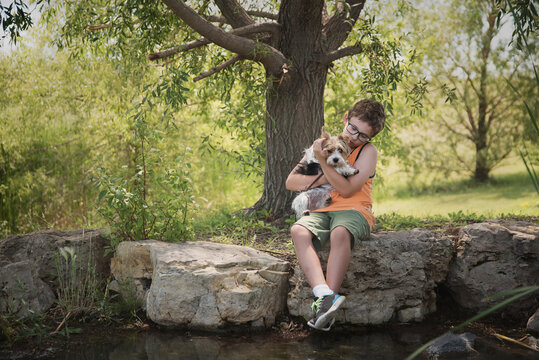 Boy with Yorkshire Terrier sitting on rock by pond at park
