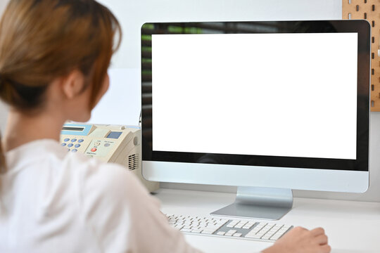 View over shoulder of young creative woman looking at white blank computer monitor.