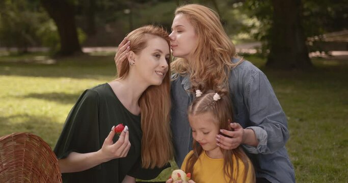 Young lgbtq couple with daughter enjoying a picnic