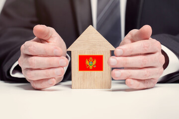 Businessman hand holding wooden home model with Montenegro union flag. insurance and property concepts