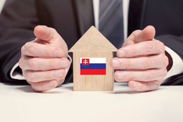 Businessman hand holding wooden home model with Slovakian flag. insurance and property concepts