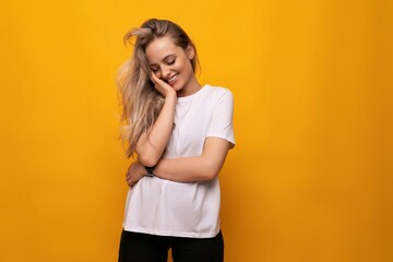 shy blond girl in a white T-shirt on a yellow background