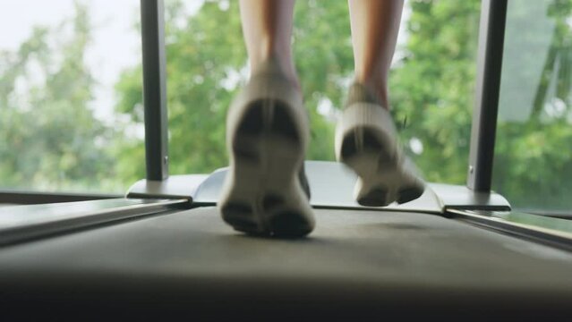 Close-up female legs in sportswear and running shoe of young Asian female runner cardio running on techno machine treadmill start morning routine lifestyle exercise in fitness gym at sport club.