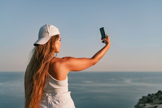 Selfie woman in cap and tank top making selfie shot mobile phone post photo social network outdoors on sea background beach people vacation lifestyle travel concept.