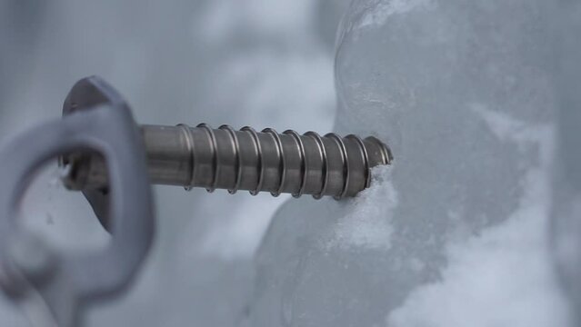 An Ice Climber sets an Ice Screw  into a frozen waterfall