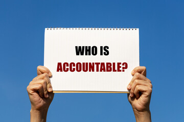 Who is accountable text on notebook paper held by 2 hands with isolated blue sky background. This message can be used as business concept to ask audience who is accountable.