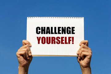 Challenge yourself text on notebook paper held by 2 hands with isolated blue sky background. This message can be used as business concept to encourage audience challenging yourself.