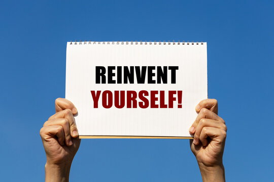 Reinvent Yourself Text On Notebook Paper Held By 2 Hands With Isolated Blue Sky Background. This Message Can Be Used As Business Concept To Encourage Audience Reinventing Yourself.