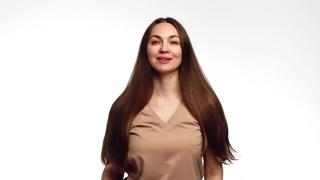 Young beautiful caucasian woman smiling and shaking her healthy shiny brown hair with both hands on white background. Attractive woman flirty touches her hair by the hand