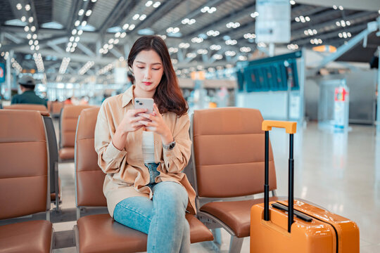 Serious asian tourist woman using mobile smartphone with suitcase traveling between waits for flight in Airport Terminal, Browse Internet, flight check in, Tourist journey trip concept