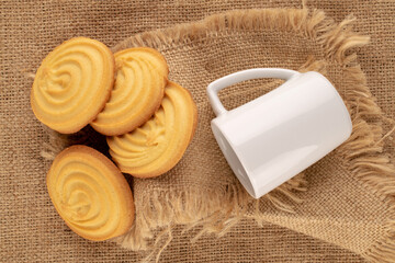 Fototapeta na wymiar Four sweet cookies with white ceramic cup on jute cloth, macro, top view.
