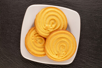 Three sweet cookies on white ceramic saucer, on slate stone, macro, top view.