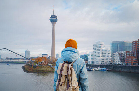 autumn or winter travel to Dusseldorf, Germany. young Asian tourist or student in blue jacket and yellow hat ( symbol of Ukraine) walks through sights of European city. beautiful view in the Media Bay