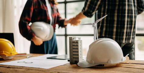Construction team shake hands greeting start new project plan behind yellow helmet on desk in office center to consults about their building project.